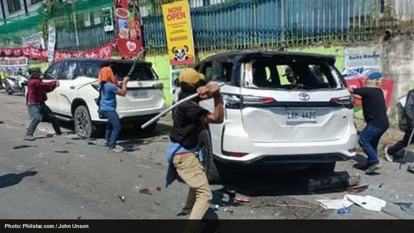 Men swing poles at two white SUVs parked on a Cotabato City street during BARMM election violence.