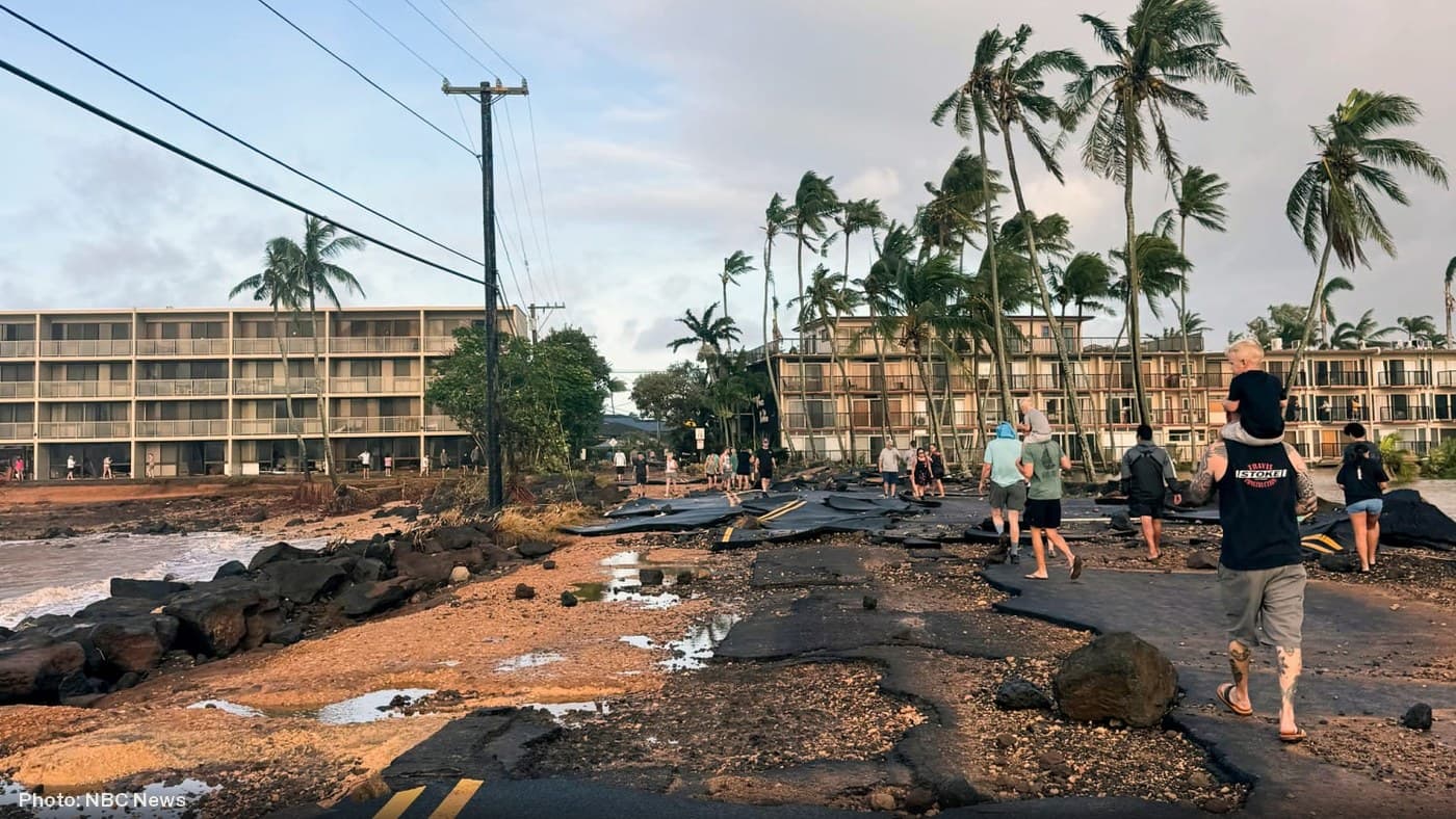 Residents walk past a road destroyed by storm surge from Hurricane Lowell in Po'ipu, Kaua'i.