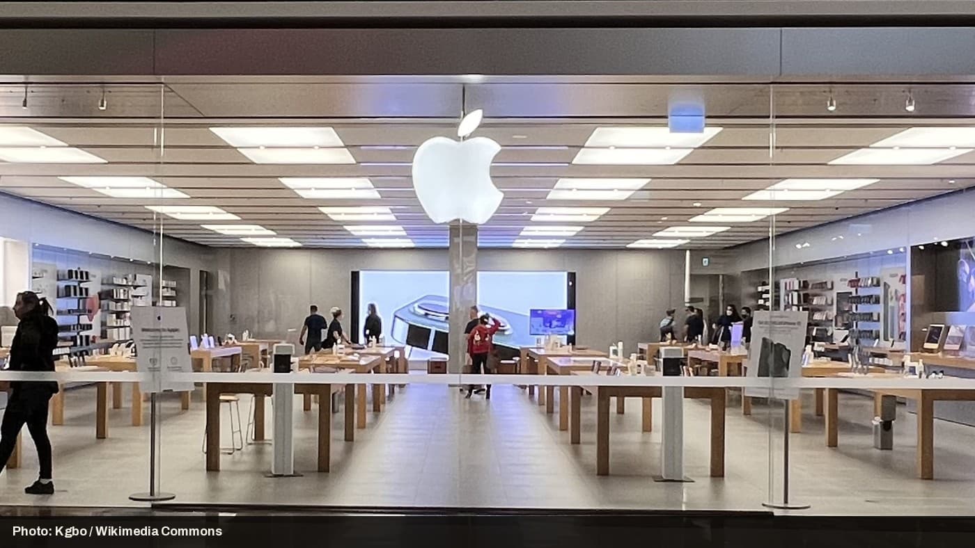The interior of an Apple Store, with customers browsing display tables.
