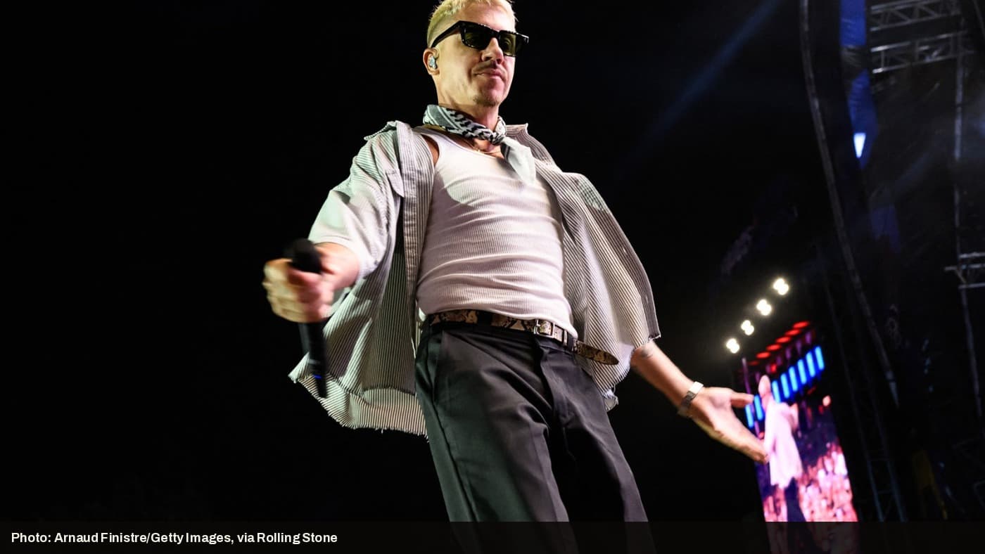 Macklemore performs on stage wearing a keffiyeh-patterned scarf.