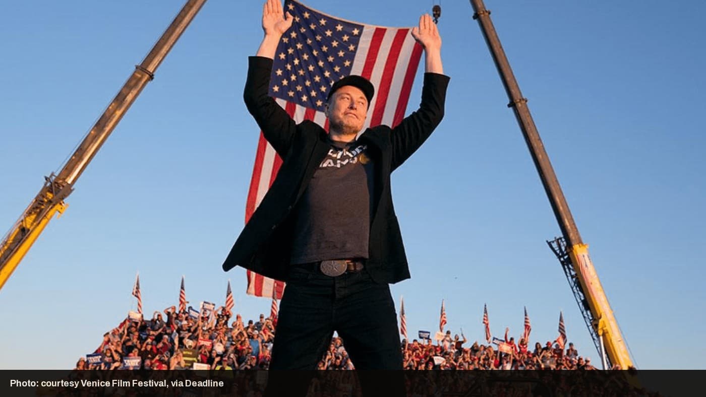 Elon Musk holds an American flag on stage at a rally, a still from the documentary "Musk."