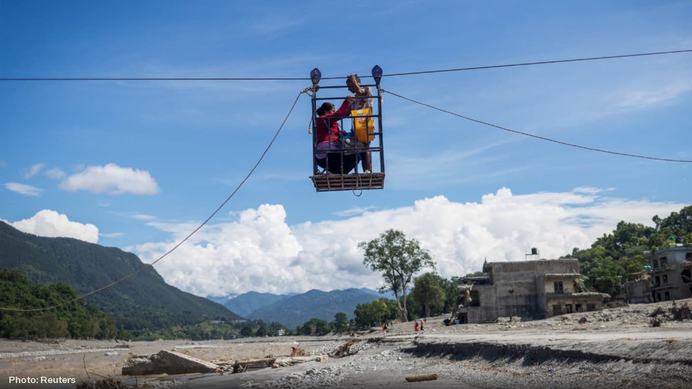 Flood survivors are carried across a devastated river valley in Nepal using a makeshift cable crossing.