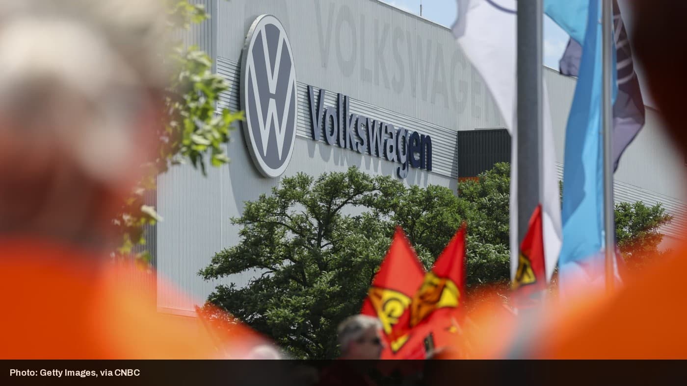 The Volkswagen logo on a factory building, with union flags visible in the foreground.