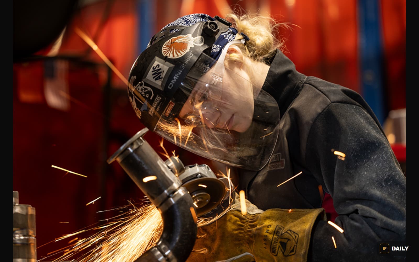 Mikala Sposito wearing a welding helmet, grinding a metal pipe with sparks flying