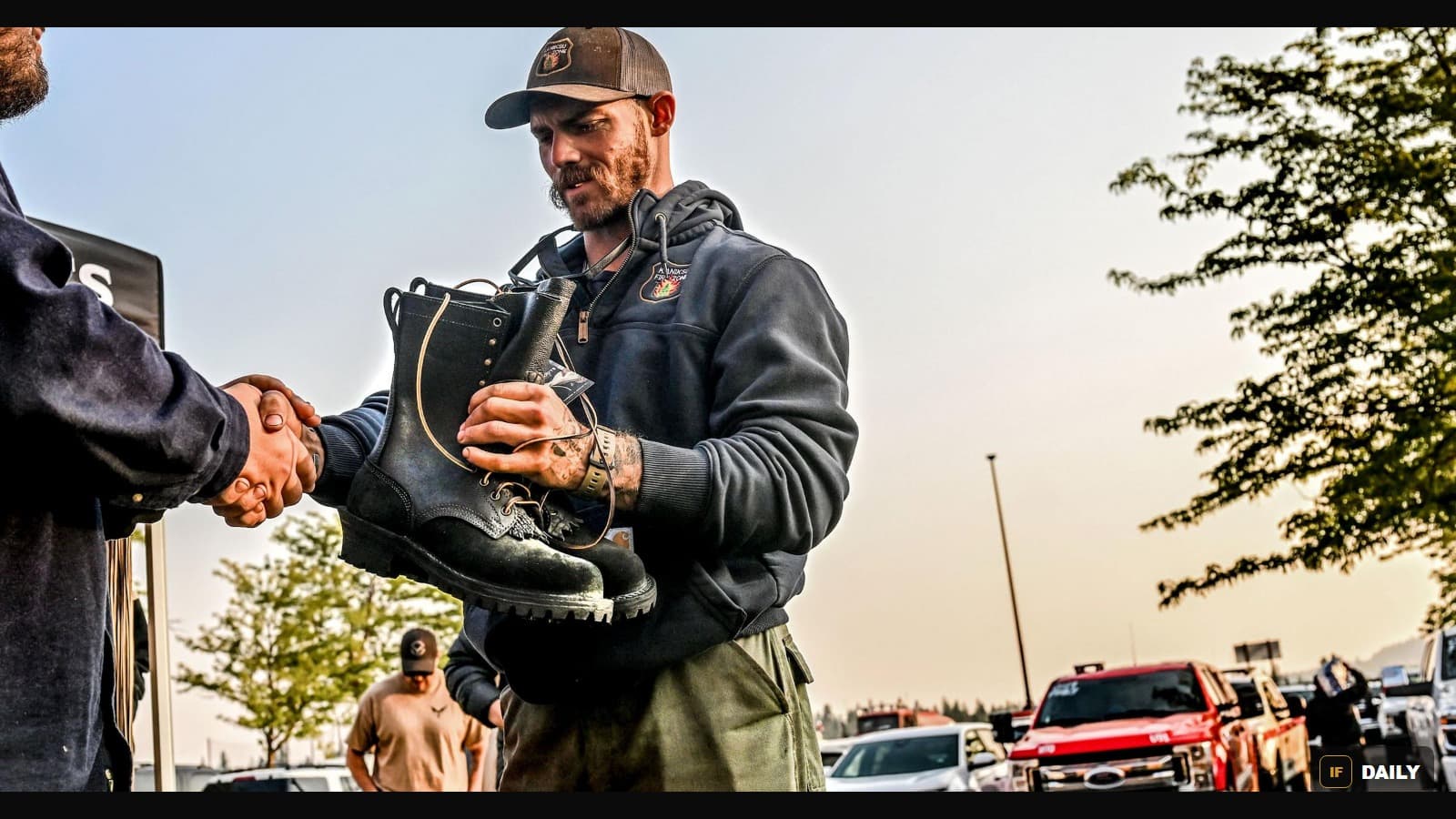 A wildland firefighter hands a worn pair of boots to a JK Boots representative while shaking hands