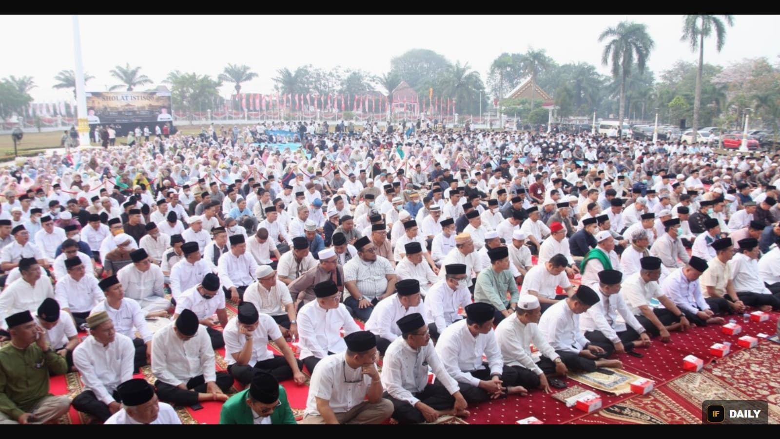 A large crowd of people in white clothing kneeling in prayer outdoors in Indonesia