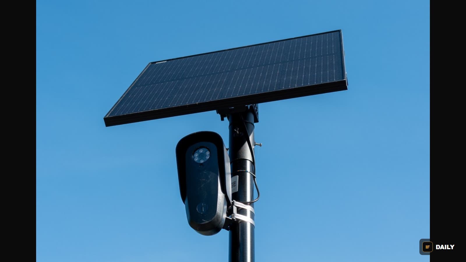 A Flock camera mounted on a pole with a solar panel against a clear blue sky