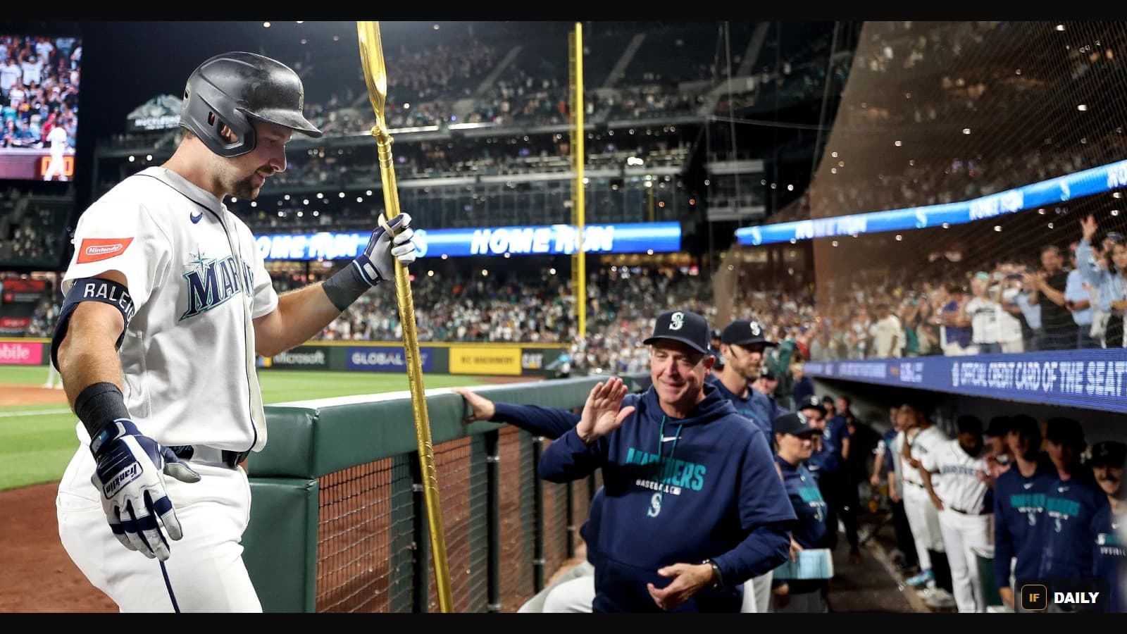Cal Raleigh being congratulated in the dugout with a golden bat prop, with a HOME RUN scoreboard message in the background