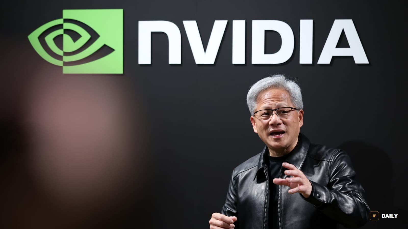 Nvidia CEO Jensen Huang speaking in front of a large Nvidia logo, wearing his signature leather jacket