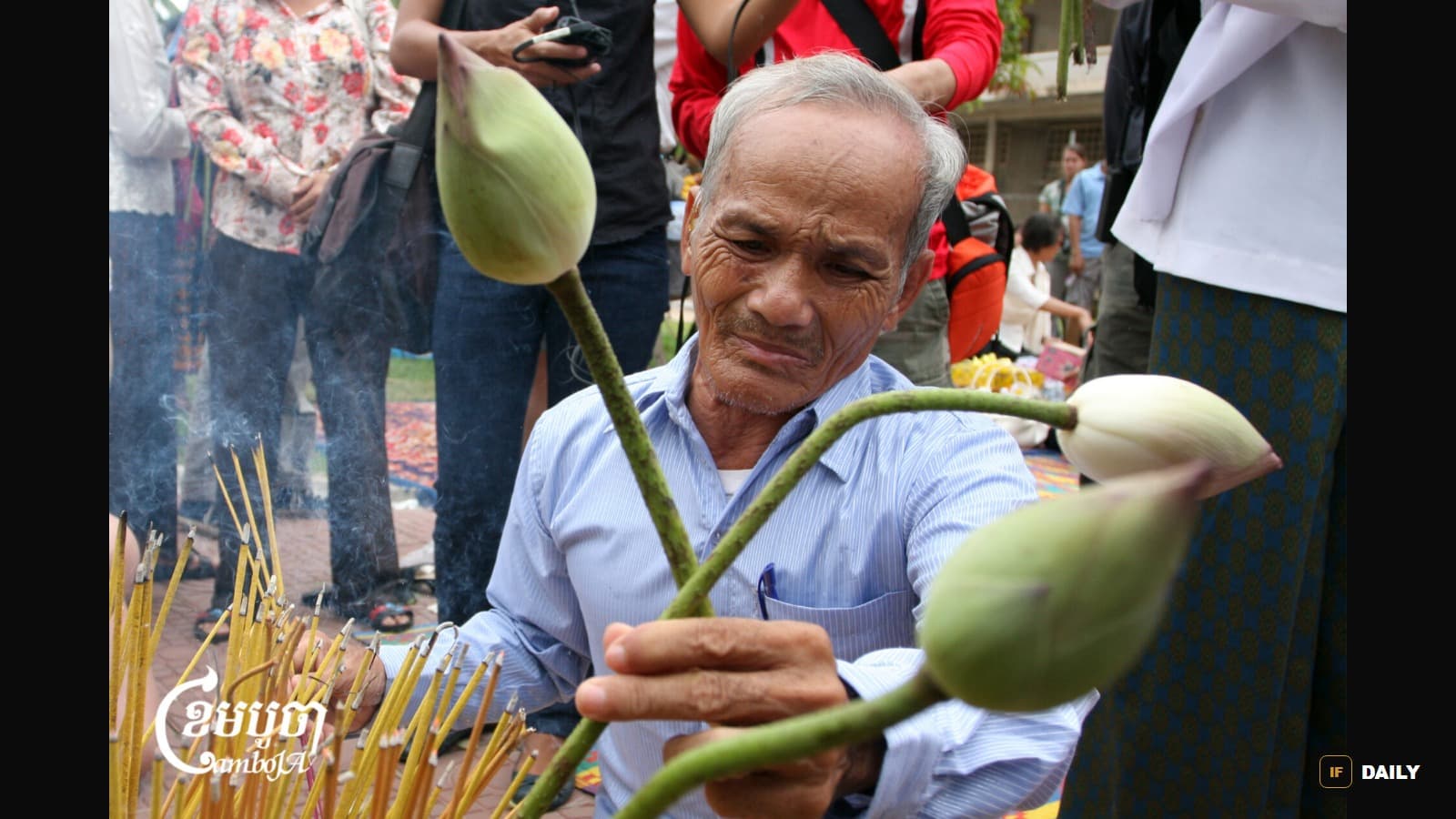 Bou Meng holding lotus flowers and incense sticks at a memorial ceremony