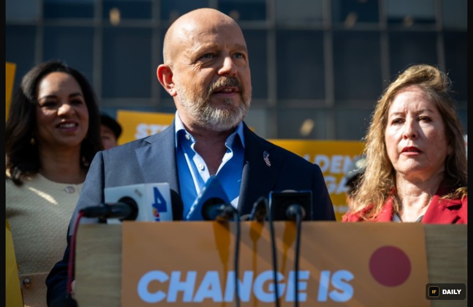 Steve Hilton speaking at a podium reading "Change Is" surrounded by supporters