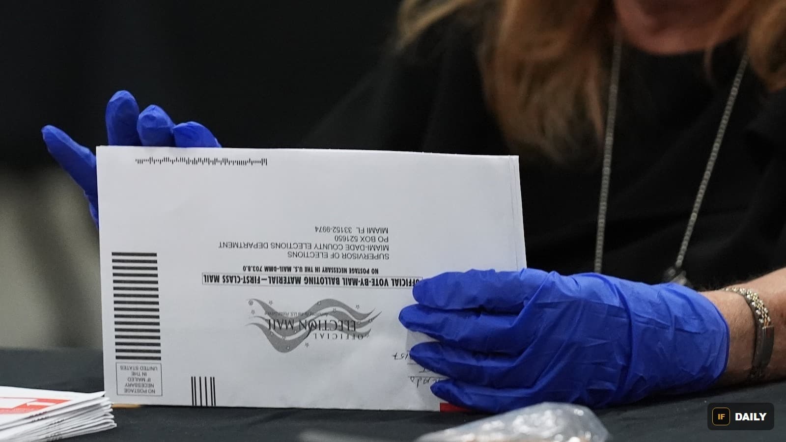 A gloved hand holding an official vote-by-mail ballot envelope from the Miami-Dade County Elections Department