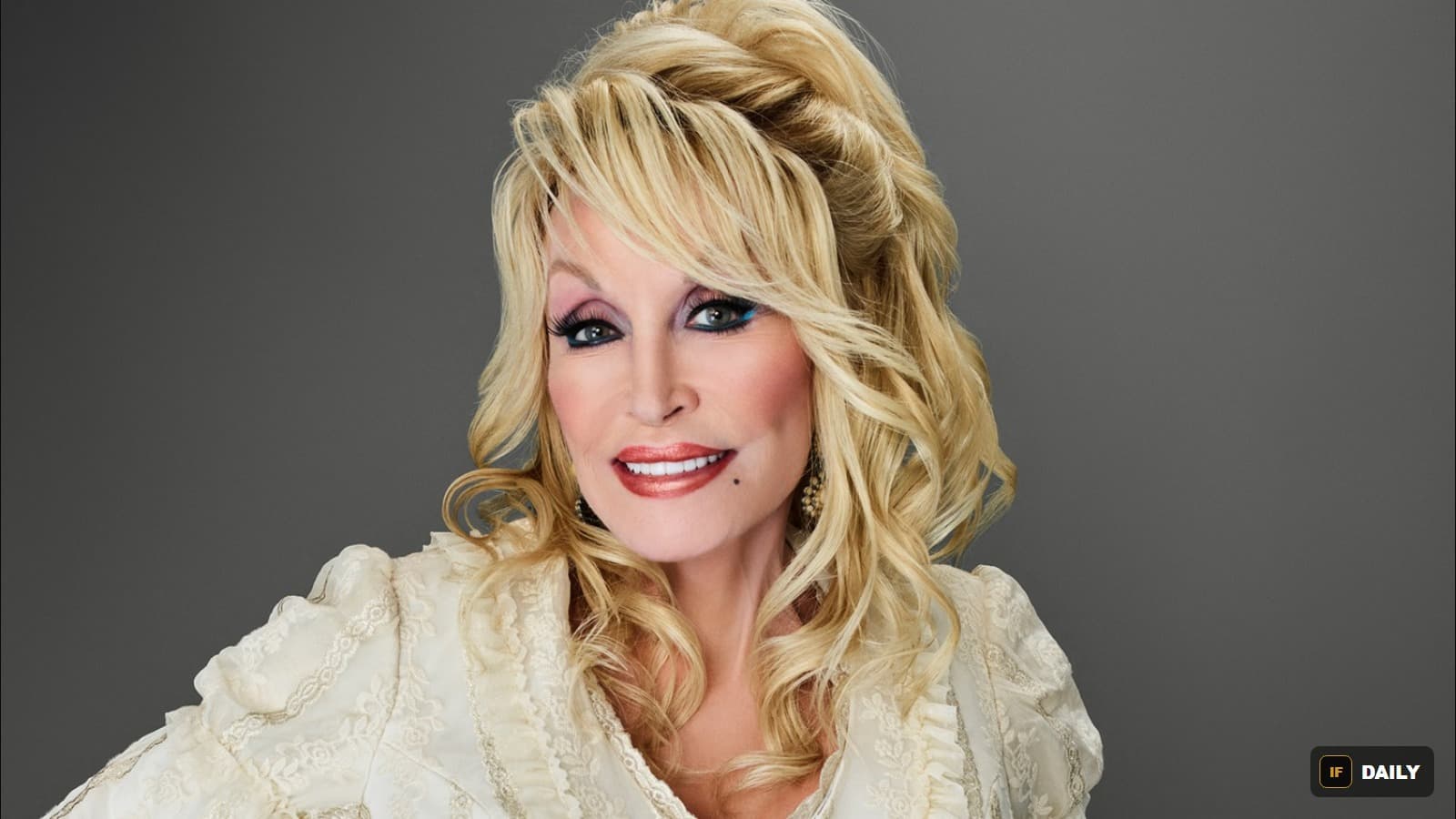 Official portrait of Dolly Parton smiling, wearing an ornate cream-colored lace outfit with her signature blonde hair