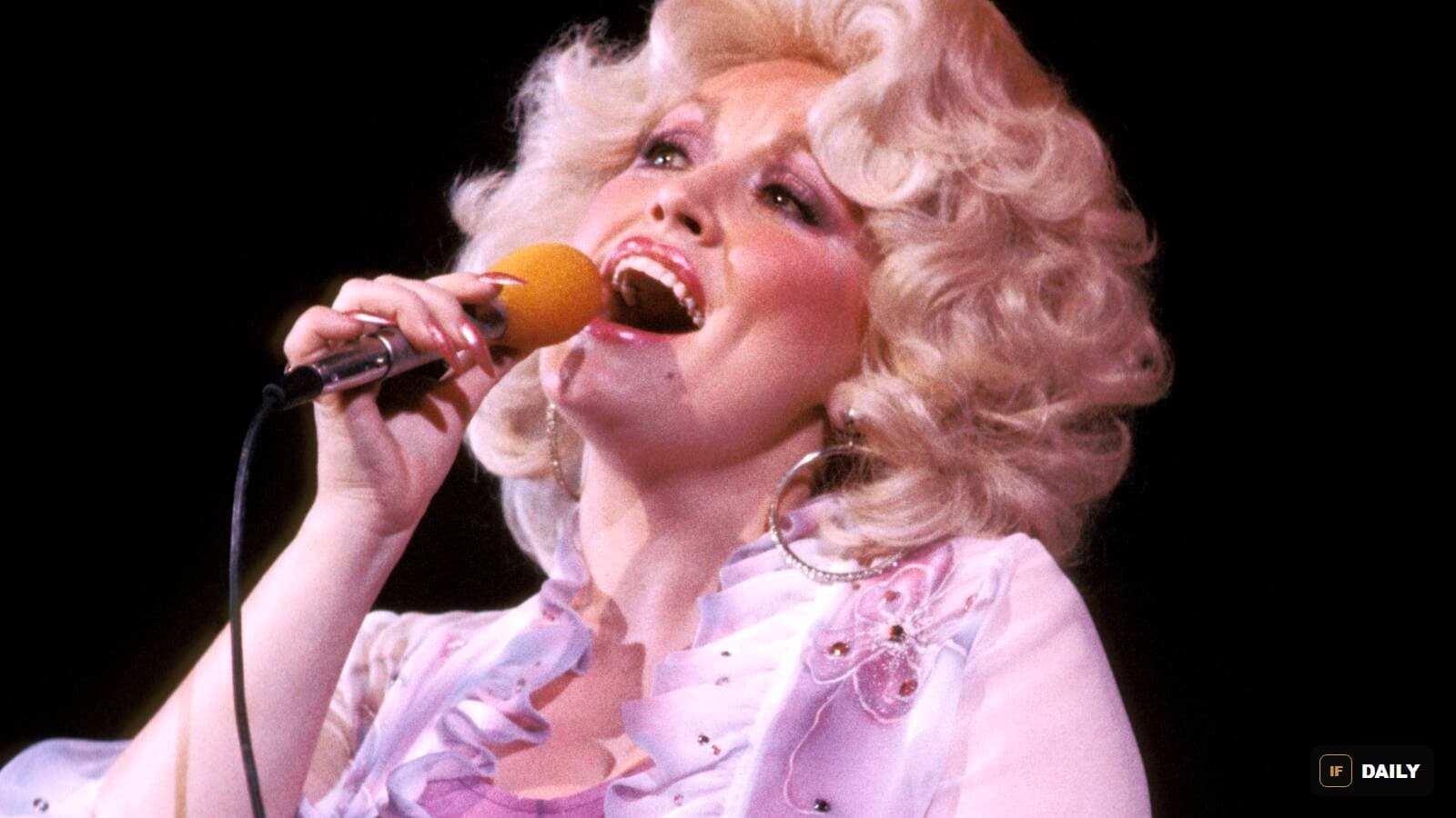 Dolly Parton singing into a microphone on stage in a ruffled lace outfit with large hoop earrings