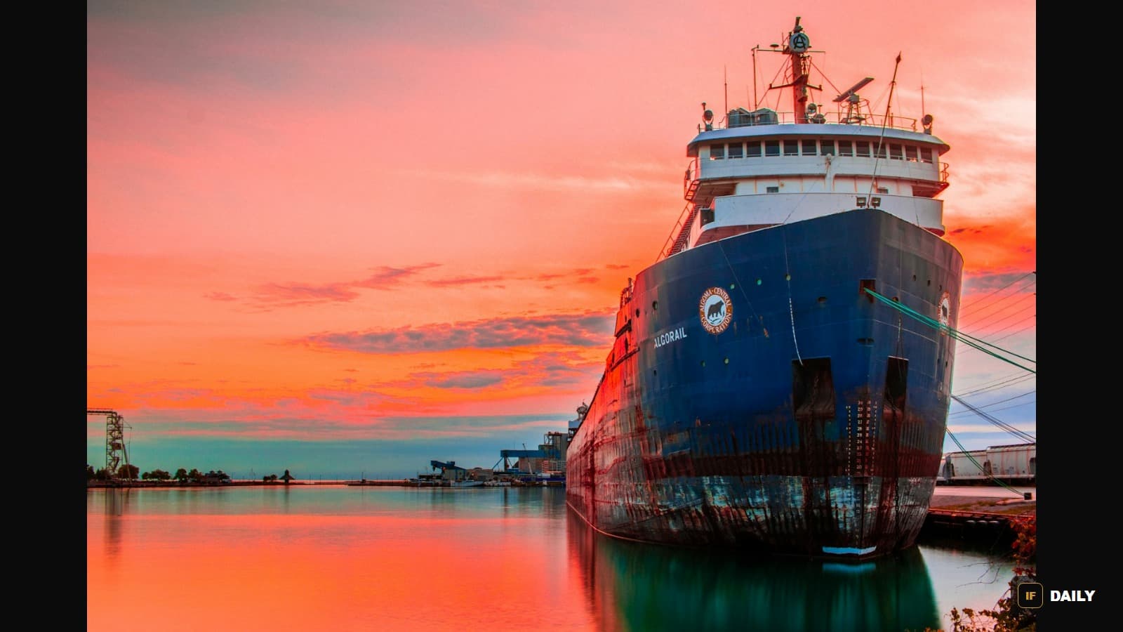 A large blue oil tanker docked at a port at sunset, its hull reflecting in calm water
