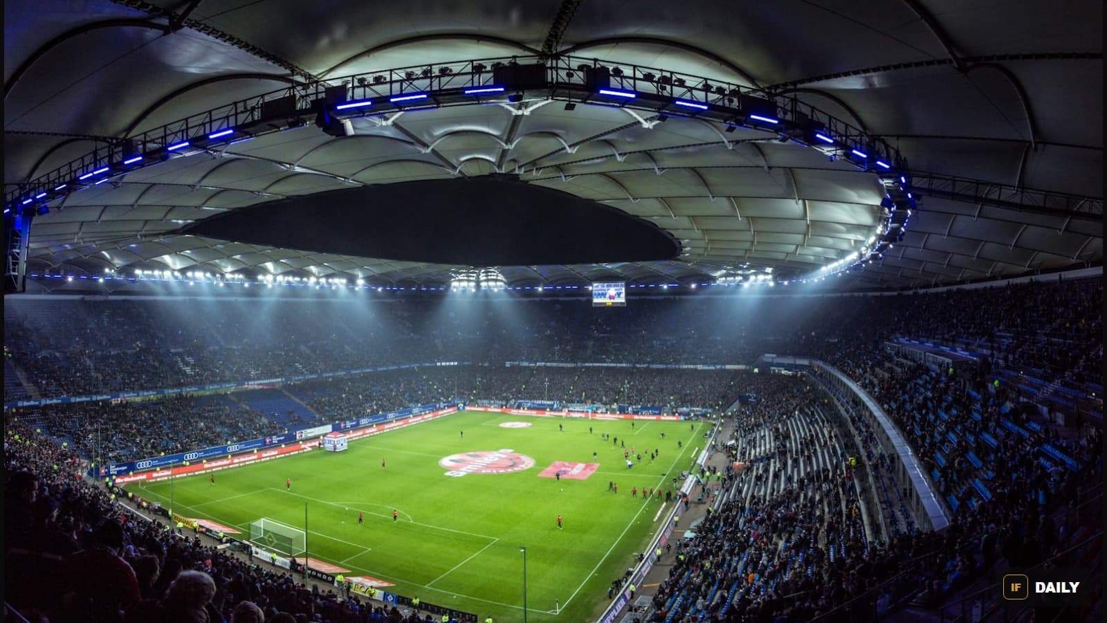 A packed, brightly lit football stadium viewed from above during a night match