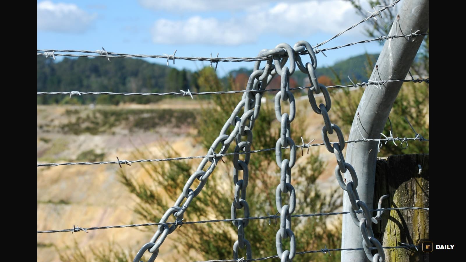 A chain-link and barbed-wire fence in front of an open field