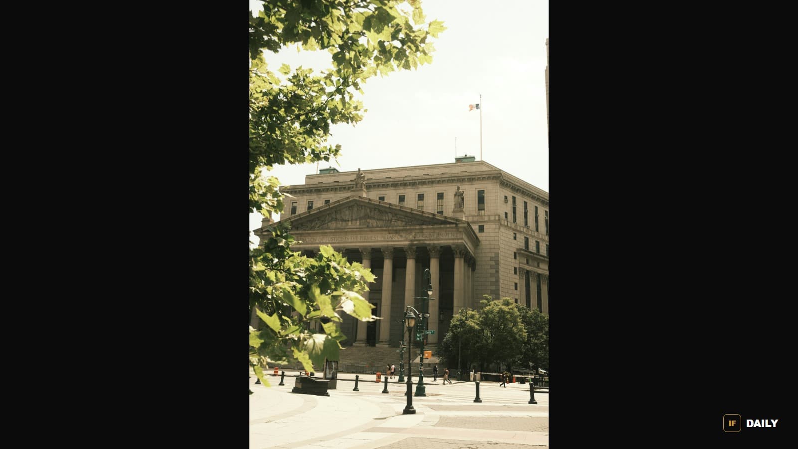 A large stone courthouse building with tall classical columns, viewed from a plaza with tree branches in the foreground