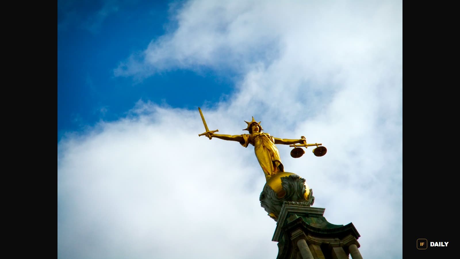A statue of the scales of justice held aloft against a cloudy sky