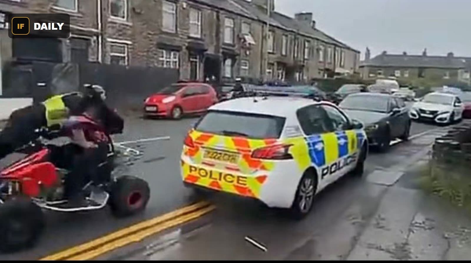 A quad bike with two riders passes close to a marked UK police car on a residential terraced street
