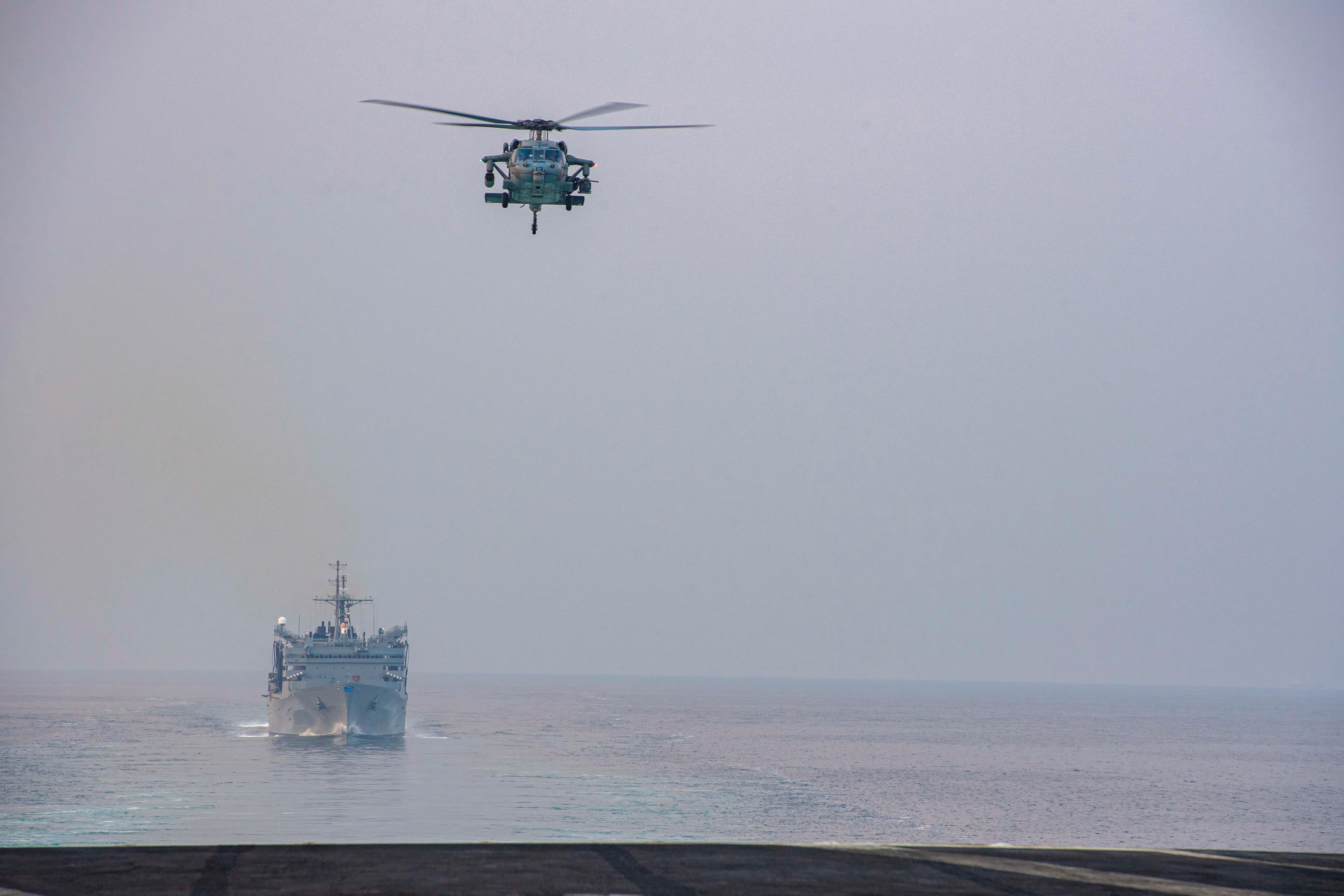 A U.S. Navy helicopter flies over a warship transiting the Strait of Hormuz