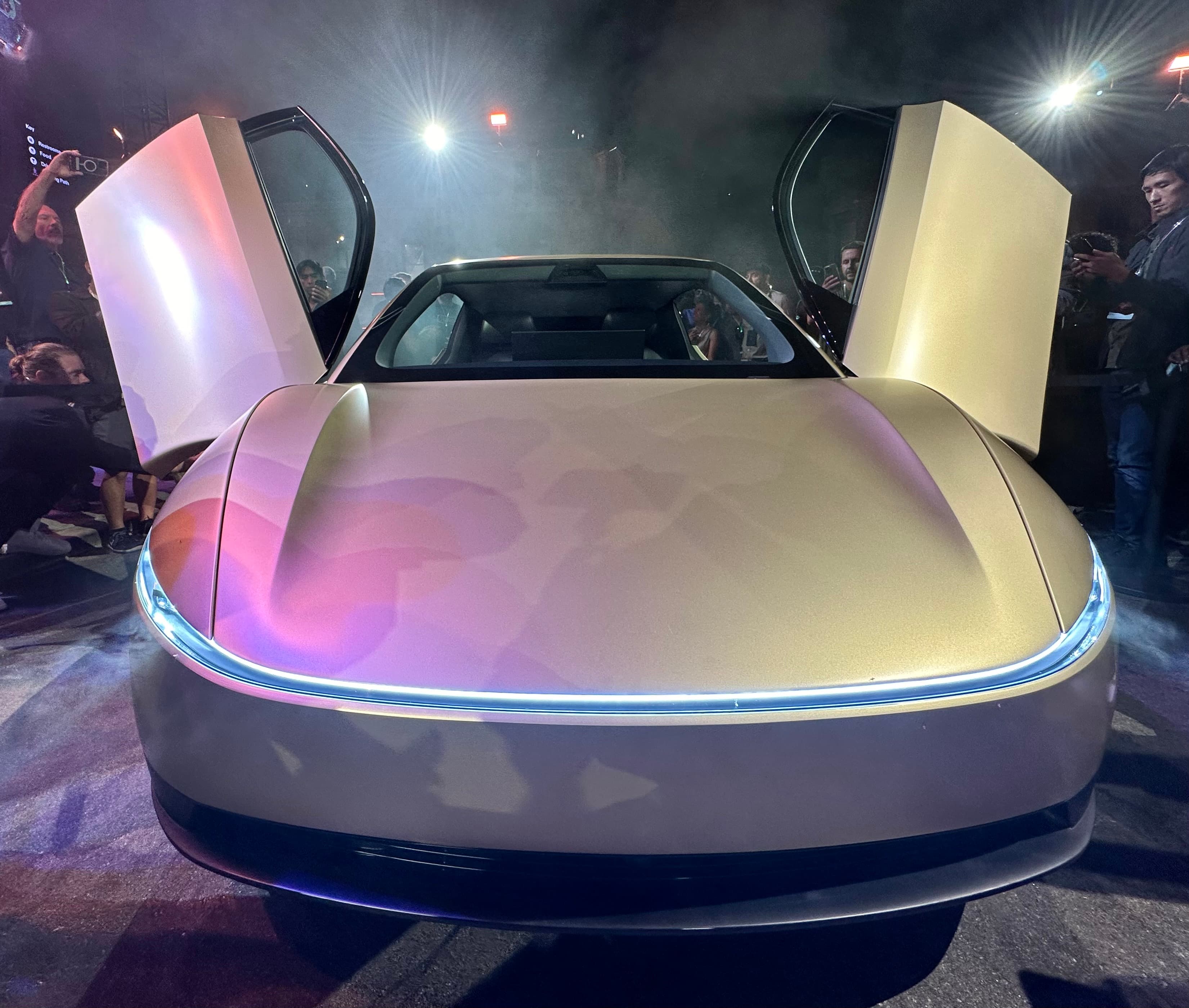 A Tesla Cybercab with its front doors open at a launch event, surrounded by onlookers