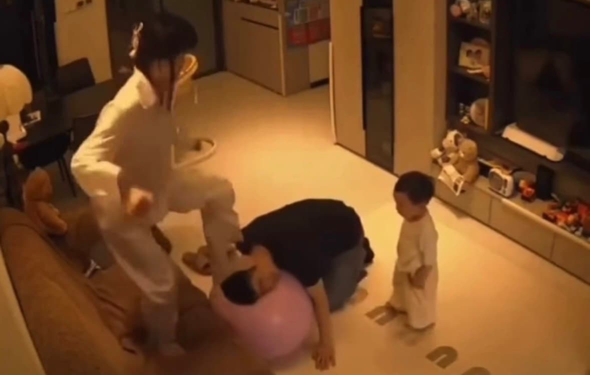 Father playing with toddler on exercise ball in living room as mother walks in viral video