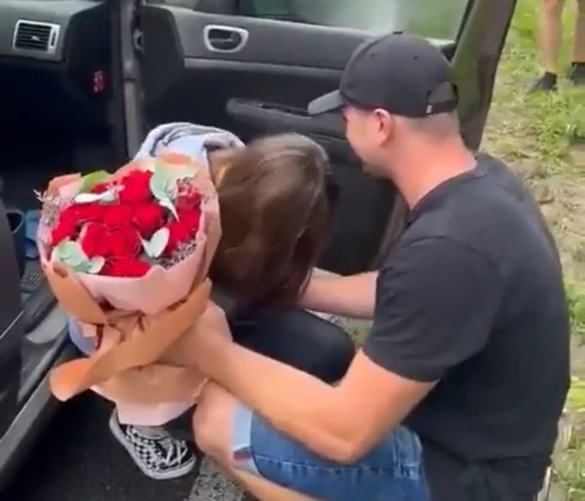 A woman cries inside a car as her boyfriend approaches with flowers after a staged abduction proposal