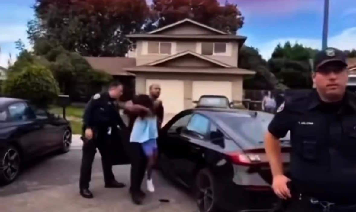 Police officers stand beside vehicles during the removal of a child as family members watch