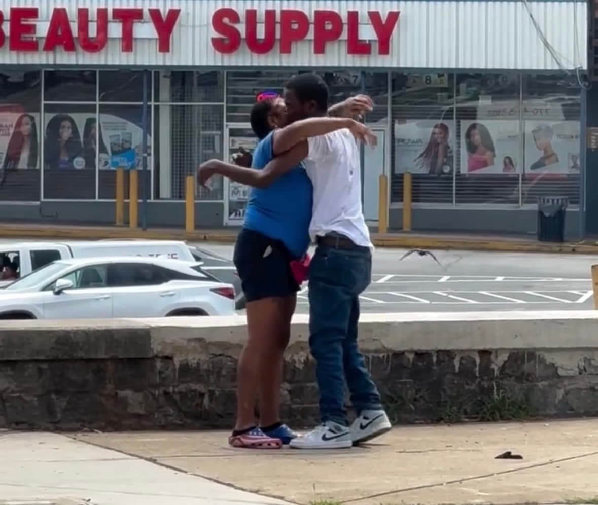 Two people involved in a public fight on a sidewalk while another man stands nearby watching