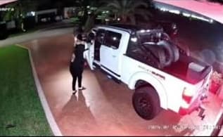 A person standing beside a white Shelby Raptor pickup truck at night as an apparent theft attempt unfolds